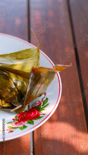 Traditional Indonesian pepes ayam food wrapped in banana leaf served on a vintage floral plate.