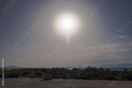 Принти на полотні Bright sun over a dry coastal landscape with water and distant mountains
