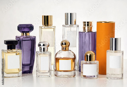 Several decorative fragrance bottles are displayed in a studio arrangement, featuring clear glass, colorful liquids, metallic caps, and distinctive geometric designs.