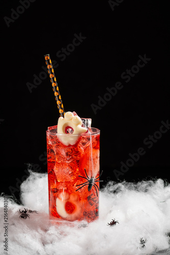 Spooky Halloween Cocktail with Ice Cubes and Ghost Garnish Decorated with Fake Spiders and Cobwebs