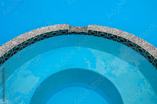 Swimming pool with peeling blue paint and worn plaster on curved steps, pool maintenance and resurfacing concept