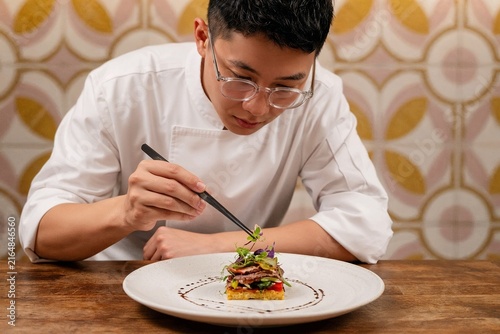 Young Asian chef meticulously plating a gourmet dish in a restaurant  