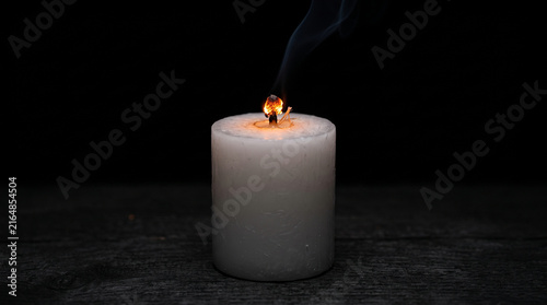 Принти на полотні Extinguished white candle with glowing ember wick and rising smoke on dark backg
