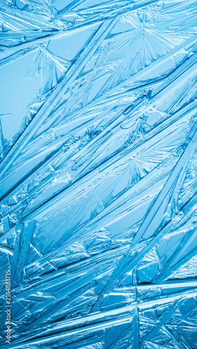 Ice frozen in intricate patterns of delicate crystals with brilliant contrasts of deep blues. Real unique patterned crystal formations. Sparkling window frost or icy cold winter frosting background.