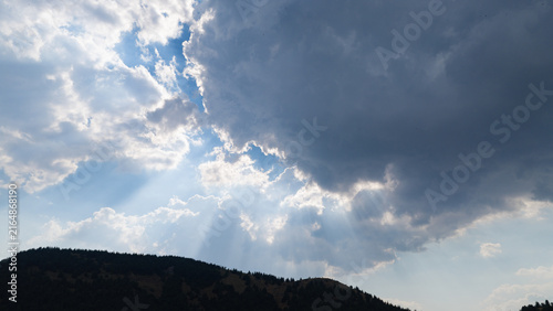Dramatic rays of sunlight filtering through the dark clouds and a view of the sky above the hills.