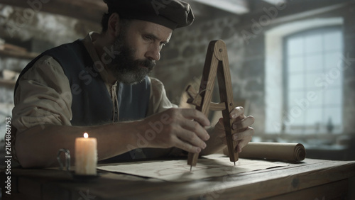 Obraz na plátně Bearded medieval inventor measuring technical dimensions on a schematic plan wit