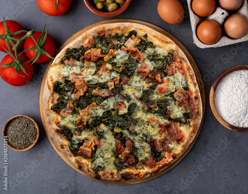 Endive, bacon and mozzarella pizza with tomatoes, eggs and flour over stone background