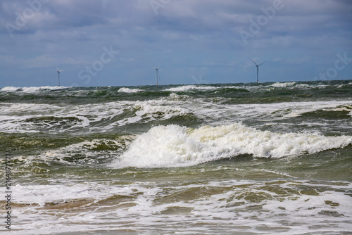 фотографія Rough North Sea Waves Breaking on a Sandy Shore with Wind Turbine