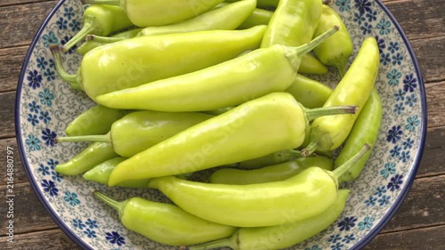 Hungarian Hot Wax peppers pile on a plate. Fresh whole light yellow and green chilies on a ceramic plate. Rustic wooden background, Table spin, backlit window light.