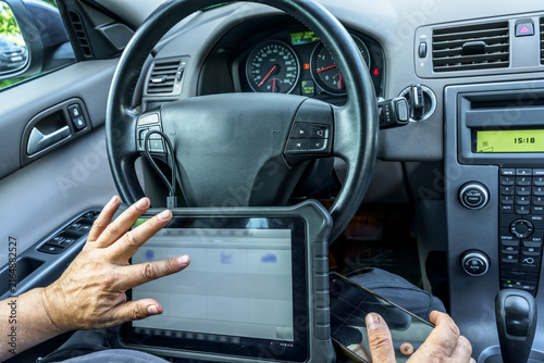 Automotive technician using diagnostic scan tool tablet computer inside a car. Pre-purchase vehicle inspection, electronics troubleshooting, and auto maintenance concept