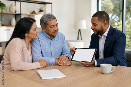 Financial advisor explaining retirement options to a diverse mature couple using a blank tablet