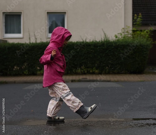 Foto A young child wearing a bright pink raincoat and waterproof pants plays joyfully in a puddle on a wet street