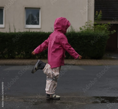 Foto A young child wearing a bright pink raincoat and waterproof pants plays joyfully in a puddle on a wet street