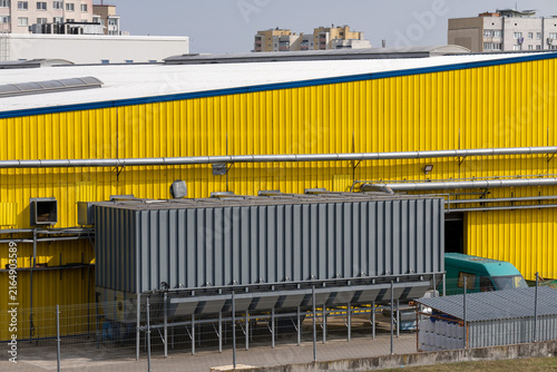 Yellow industrial warehouse facade with corrugated metal cladding, roof pipe and utility equipment