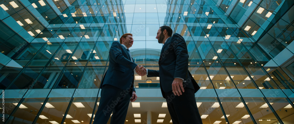Fototapeta premium Business executives shake hands in modern office atrium, symbolizing partnership, trust, agreement, success, and cooperation.