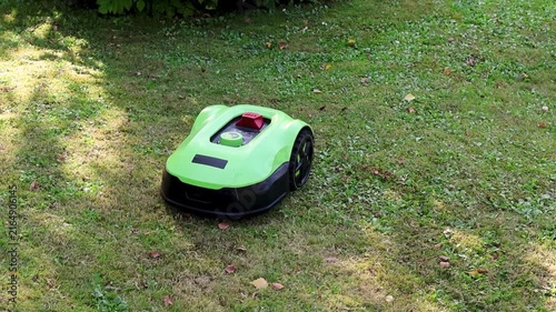 Robotic lawn mower autonomously mowing a residential garden lawn on a sunny day. Modern automatic grass cutting machine moving across a well-maintained green yard