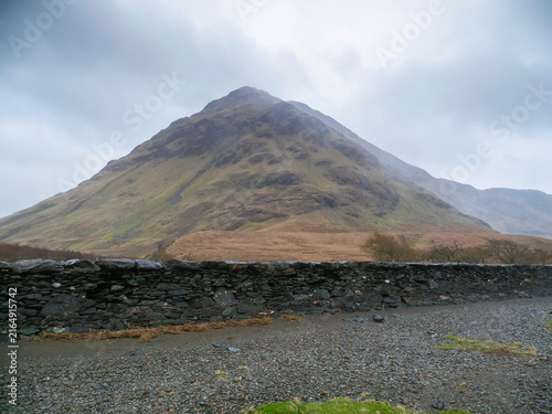 Bild auf Leinwand Large mountain rises above stone wall and gravel path