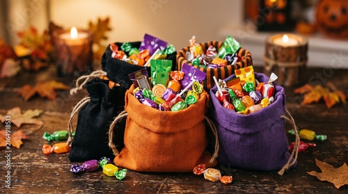 Halloween Candy Bags Filled With Assorted Sweets and Candies on a Wooden Table with Autumn Leaves and Candles