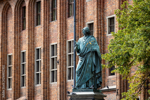 Cuadro en lienzo Bronze Copernicus Monument in Torun stands before a historic brick building with tall arched windows