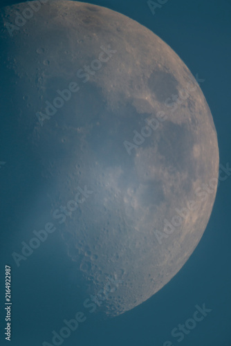 Prime focus astrophotography of half moon with surface craters in twilight blue sky Greece.