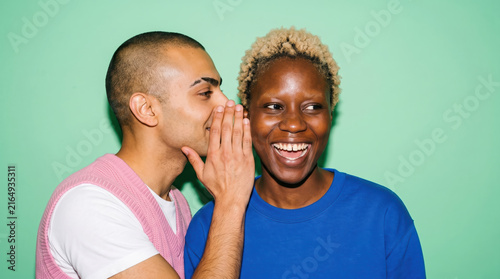 Two friends whispering a secret on a mint backdrop