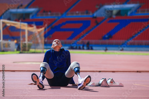Tired bilateral amputee athlete resting with head back on running track.Exhausted para-athlete with two leg prostheses taking a break near starting blocks.Disabled track runner resting eyes and breath
