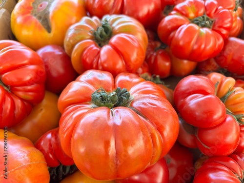 Fotografie A vibrant pile of ribbed heirloom tomatoes in rich red and orange hues, freshly