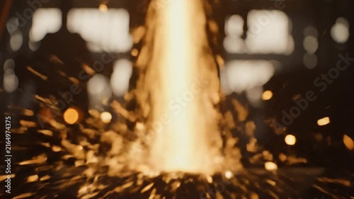 Molten metal pours down creating a spectacular shower of bright orange sparks inside a dark industrial foundry.