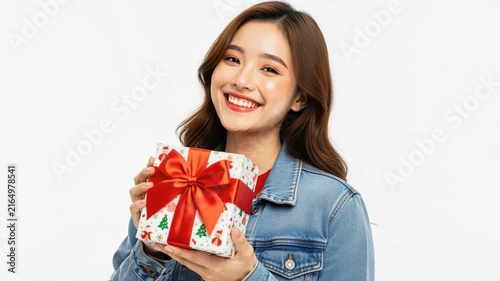 Joyful Gift Giving: A young woman with a radiant smile holds a festive Christmas gift, wrapped in patterned paper and adorned with a large red ribbon, ready to be exchanged.