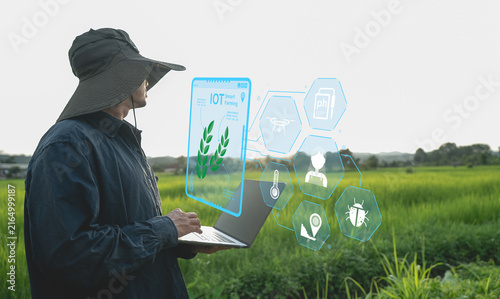 Farmer using laptop in field with digital icons representing IoT technology for smart farming
