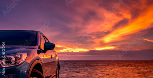 Canvastavla Blue compact SUV parked beside the ocean beneath sunset sky