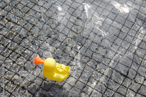 Yellow duck watering can toy floating on pool water surface