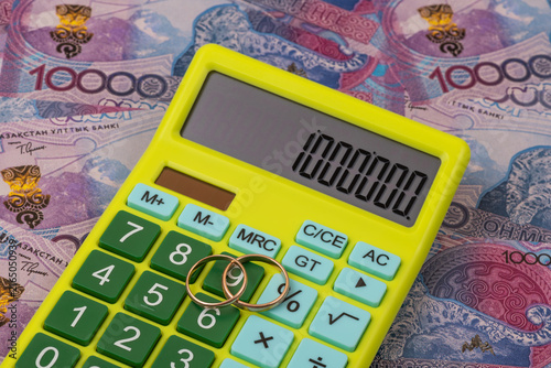 Wedding rings and a calculator against a background of 10000 Kazakhstani tenge banknotes.
