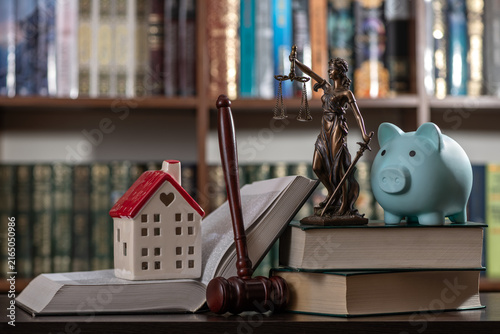 A blue piggy bank, a judge's gavel, and a figure of Themis against a backdrop of bookshelves.