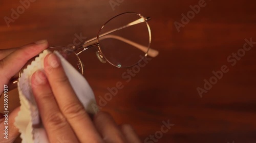 Close up shot of woman hands carefully wiping eyeglasses lenses front and back with soft microfiber cloth, vision optics care and maintenance concept.