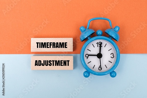 Картината върху платно Blue alarm clock with TIMEFRAME ADJUSTMENT text on wooden blocks against coloured background
