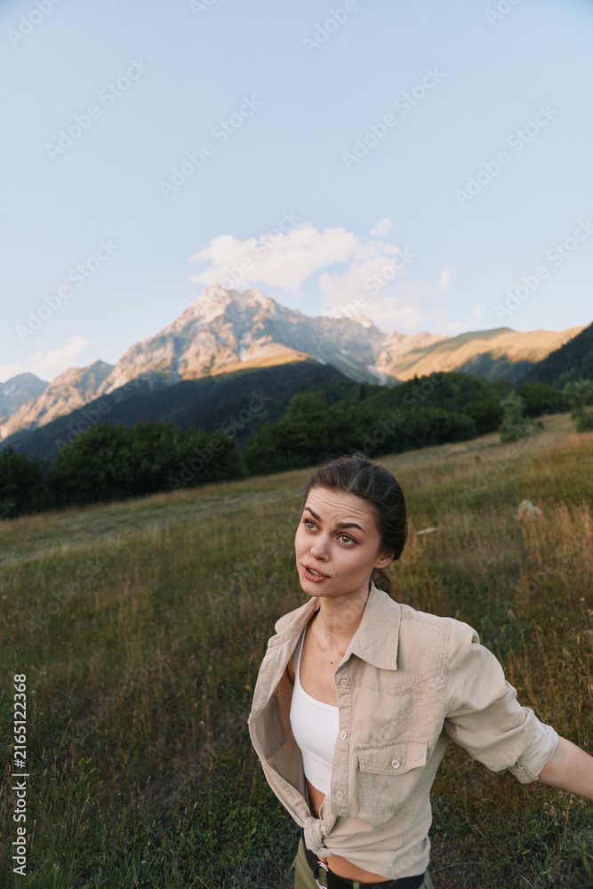 Naklejka premium Woman in casual attire stands in a meadow with distant mountains, showcasing an outdoorsy lifestyle, calm nature, and exploration under soft natural light. Warm glow.