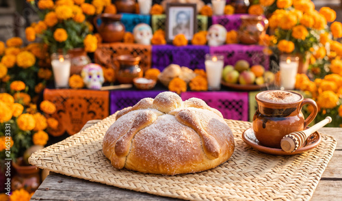 A rich round loaf of traditional Pan de Muerto on a woven straw mat (petate), Soft buttery sweet bread dusted in white sugar with dough bone shapes crisscrossing the top, served next to hot chocolate.