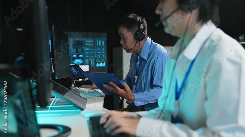 Asian operator in headset analyzes radar screens and types in a modern control room, tracking flight telemetry data.