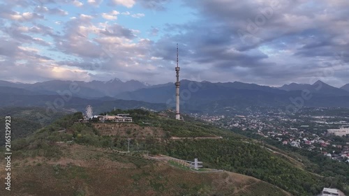 The famous TV tower on Kok Tobe Mountain in the Kazakh city of Almaty, set against a mountain range on a cloudy summer evening.
