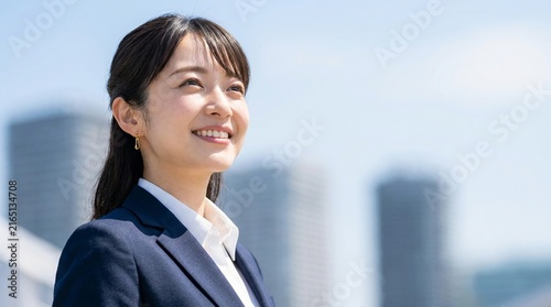 都会の高層ビル群を背に明るい笑顔で見上げる女性社員