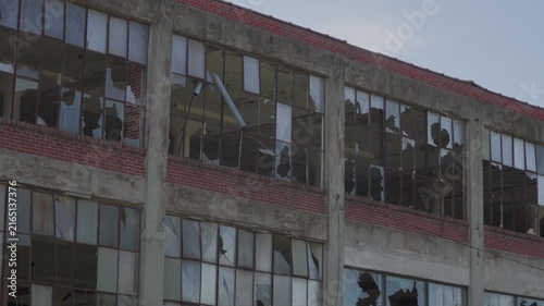 Panning shot of broken windows on the side of an abandoned warehouse. Forgotten, creepy industrial facility. Old factory.