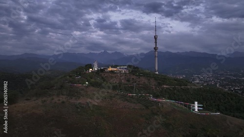 The famous TV tower on Kok Tobe Mountain in the Kazakh city of Almaty, set against a mountain range on a cloudy summer evening.