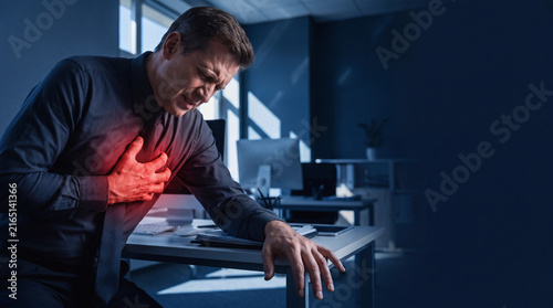 man suffering from acute myocardial infarction heart attack with chest pain in dark office