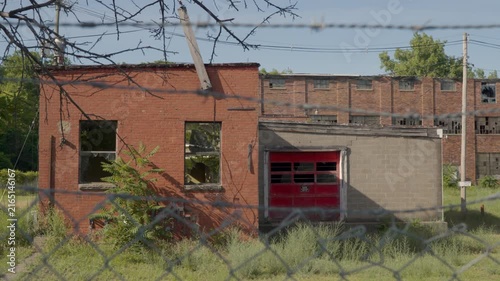 Wide shot of an abandoned factory with a broken window and a red garage door. Decaying, creepy industrial facility. 