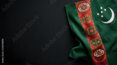 Folded Turkmenistan national flag with embroidered carpet pattern and crescent moon stars on dark fabric