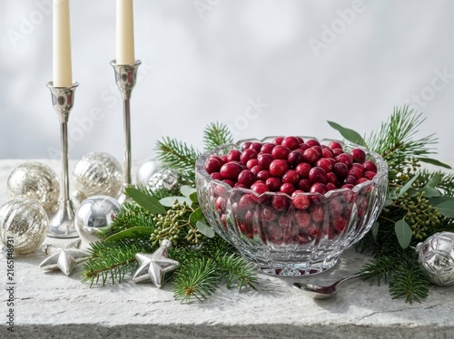 Silver bowl filled with fresh red cranberries and greenery on white table