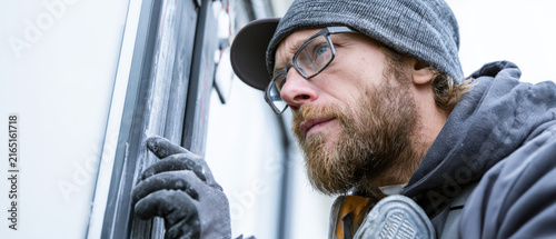 Bearded man in cap and glasses peers closely at window