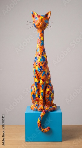 Colorful tall abstract painted cat sculpture sitting on a blue cube pedestal