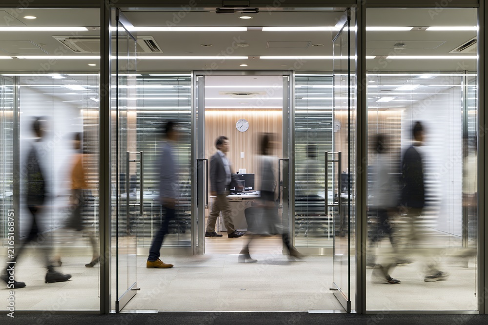 Fototapeta premium ガラス張りのオフィスを行き交うビジネスパーソンたちの忙しい日常